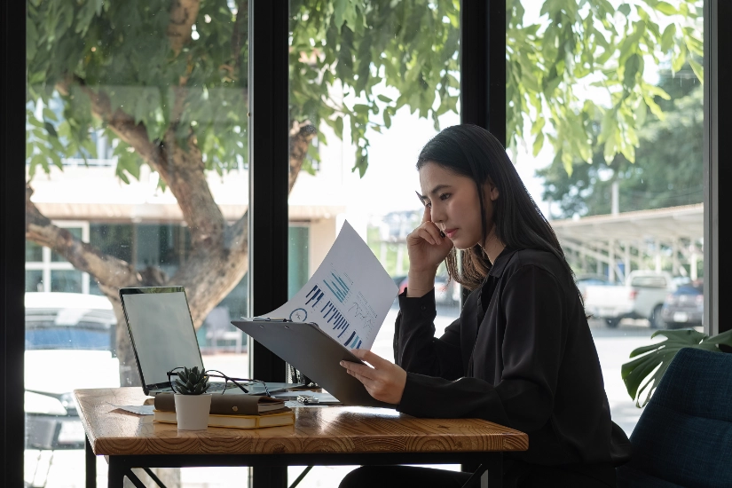 Side view young asian businesswoman sitting on her workplace in the office. Young woman working for financial document data charts with laptop in the office